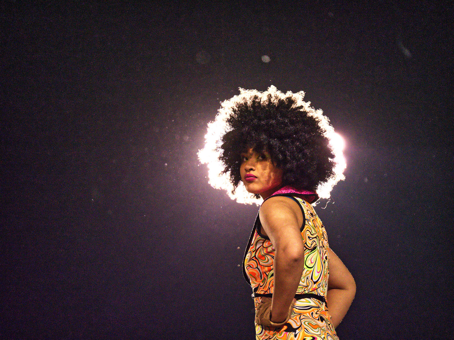 A Sound of the Swarm Mineola High School marching band color guard member’s afro is back-lit by stadium lights.